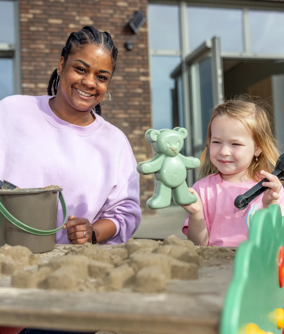 Kind speel samen met een pedagogisch medewerker in de zandbak bij kinderopvang Kind&co ludens