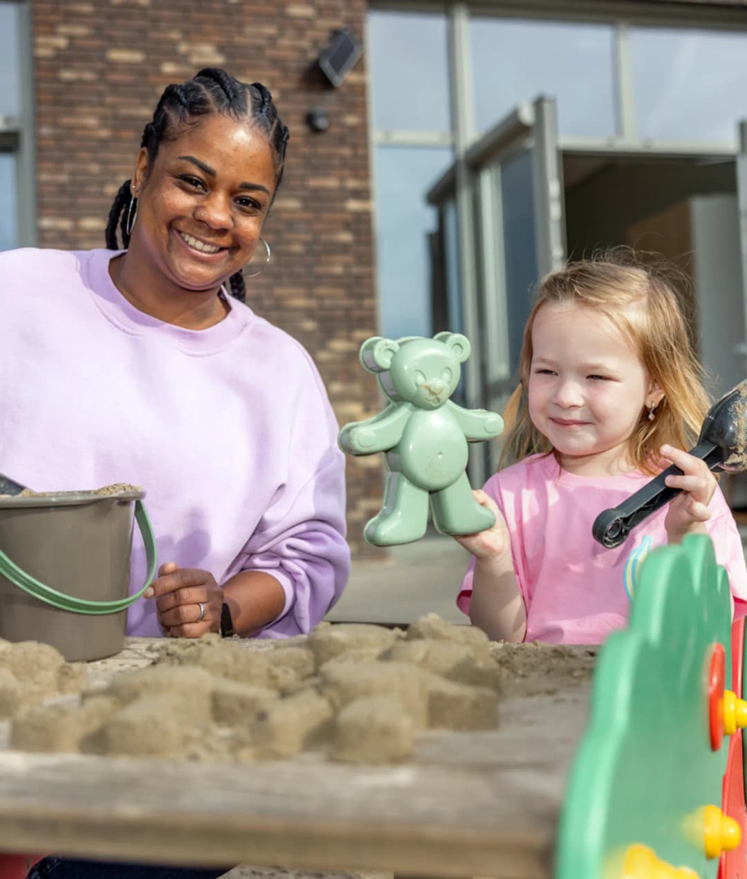 Kind speel samen met een pedagogisch medewerker in de zandbak bij kinderopvang Kind&co ludens