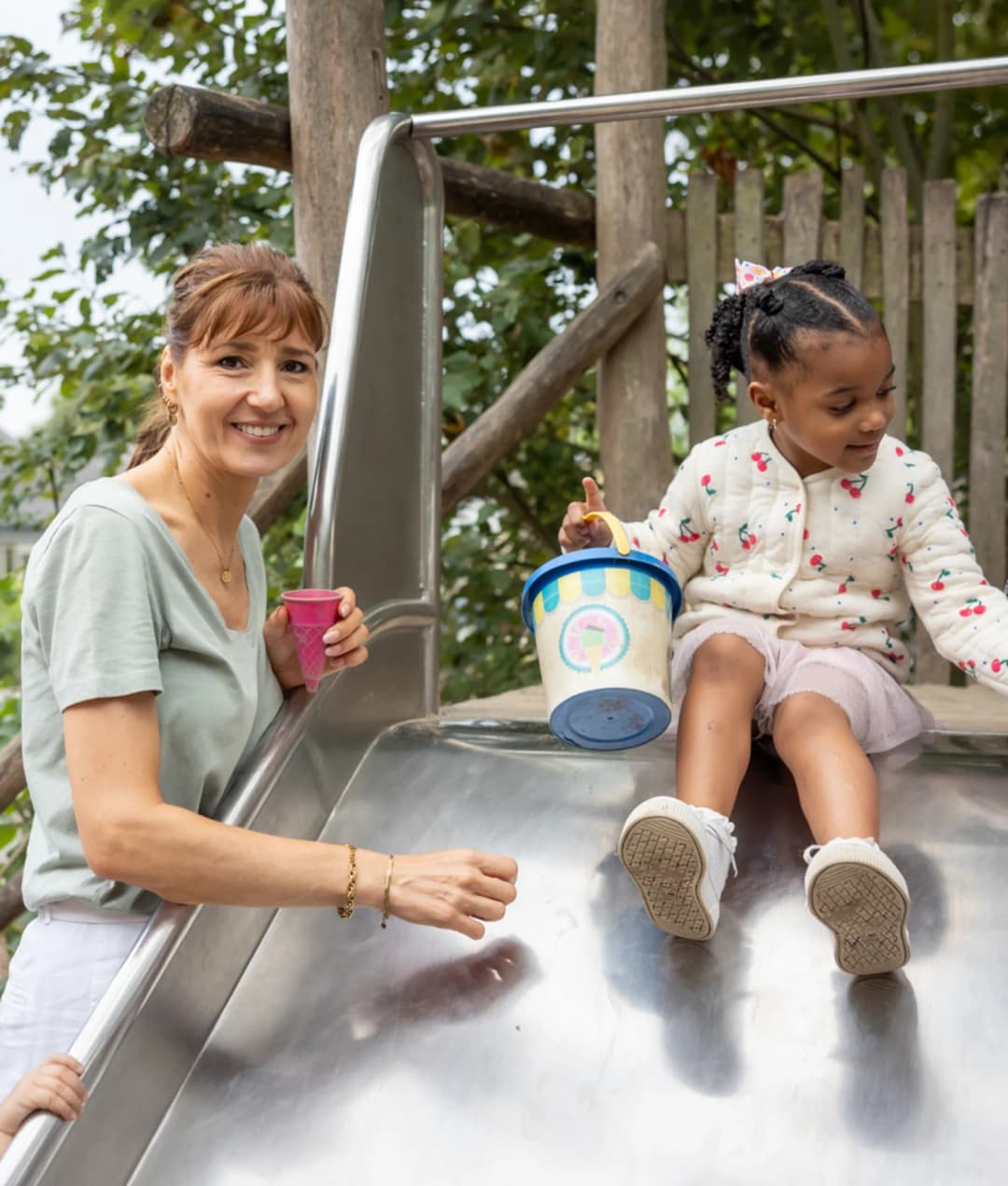 Pedagogisch medewerker staat bij kinderen die gaan glijden van de glijbaan bij kinderopvang Kind&co ludens