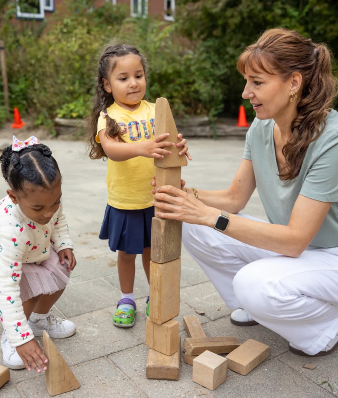 Pedagogisch medewerker bouwt buiten een houten blokkentoren met twee kinderen bij kinderopvang Kind&co ludens