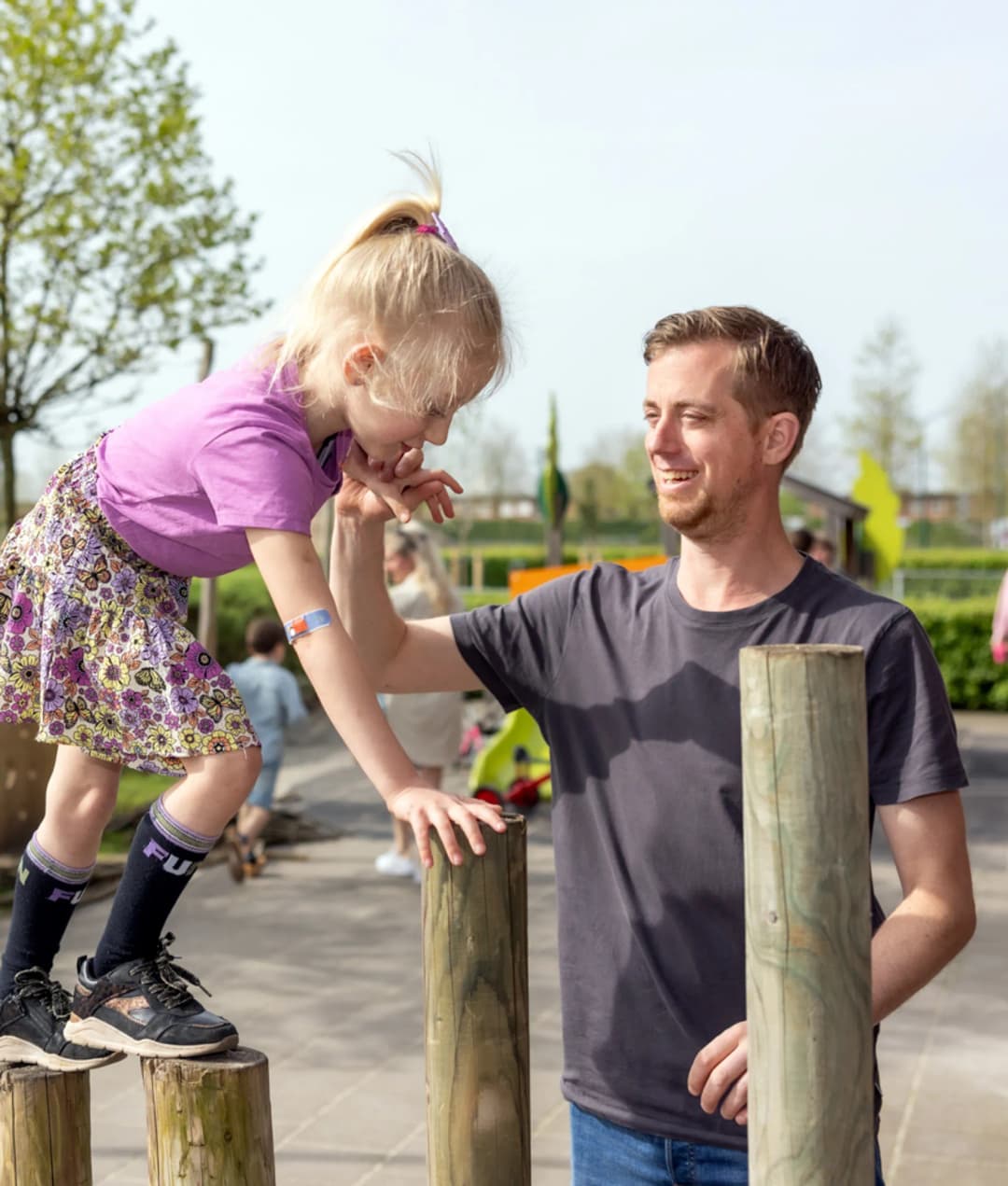kind wordt begeleid door pedagogisch medewerker bij buitenspelen op palen bij kinderopvang Kind&co ludens