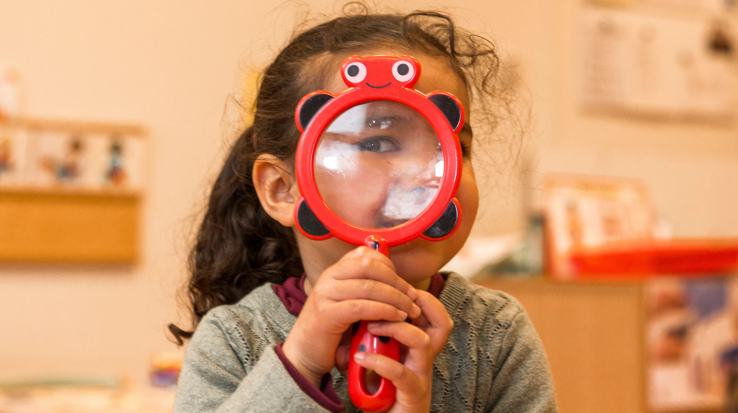 Kind op de peutergroep speelt met vergrootglas bij kinderopvang Kind&co ludens