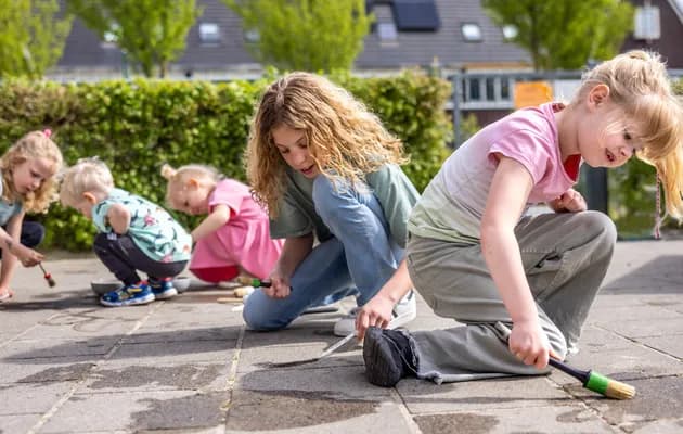 Kinderen spelen buiten op de grond met water bij kinderopvang Kind&co ludens