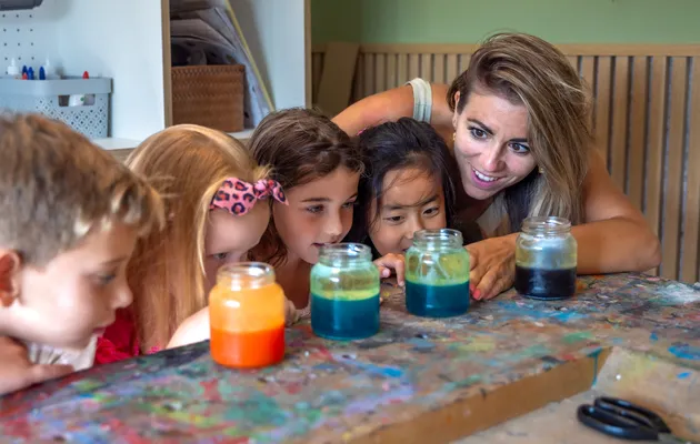 Kinderen kijken met pedagogisch medewerker naar pot met gekleurd water bij kinderopvang Kind&co ludens