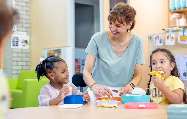 Kinderen eten samen met pedagogisch medewerker aan tafel bij kinderopvang Kind&co ludens