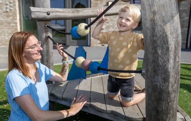 Kind klimt buiten met pedagogisch medewerker bij kinderopvang Kind&co ludens