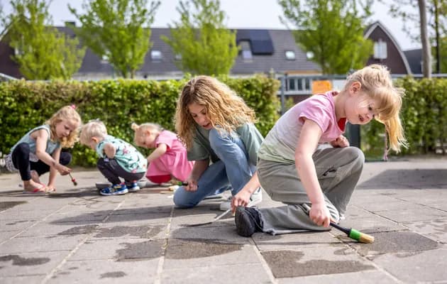 Kinderen spelen buiten op de grond met water bij kinderopvang Kind&co ludens