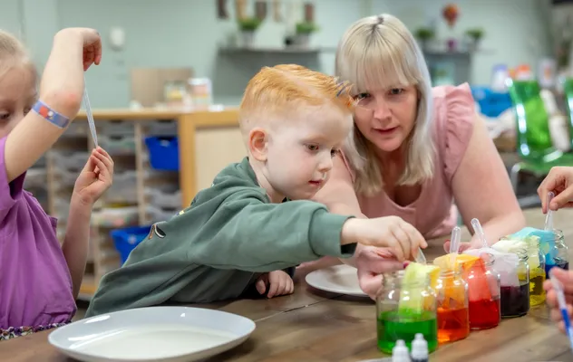 kinderen worden door een pedagogisch medewerker begeleid met het verven bij kinderopvang Kind&co ludens