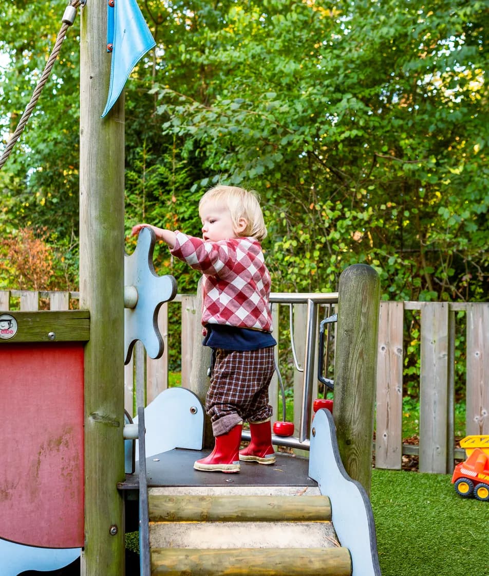 Kind speelt buiten op houten boot bij kinderopvang Kind&co ludens