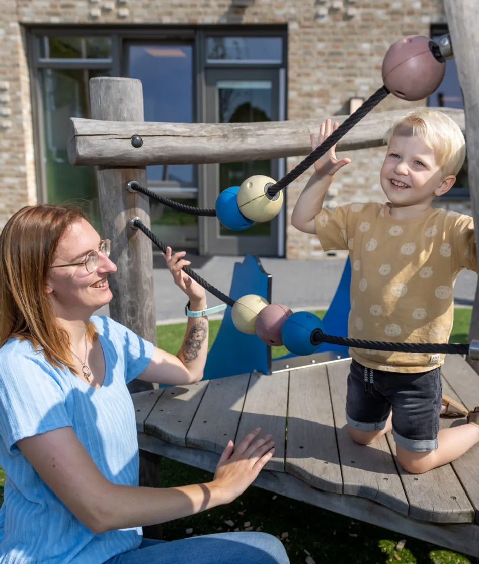 Kind klimt buiten met pedagogisch medewerker bij kinderopvang Kind&co ludens