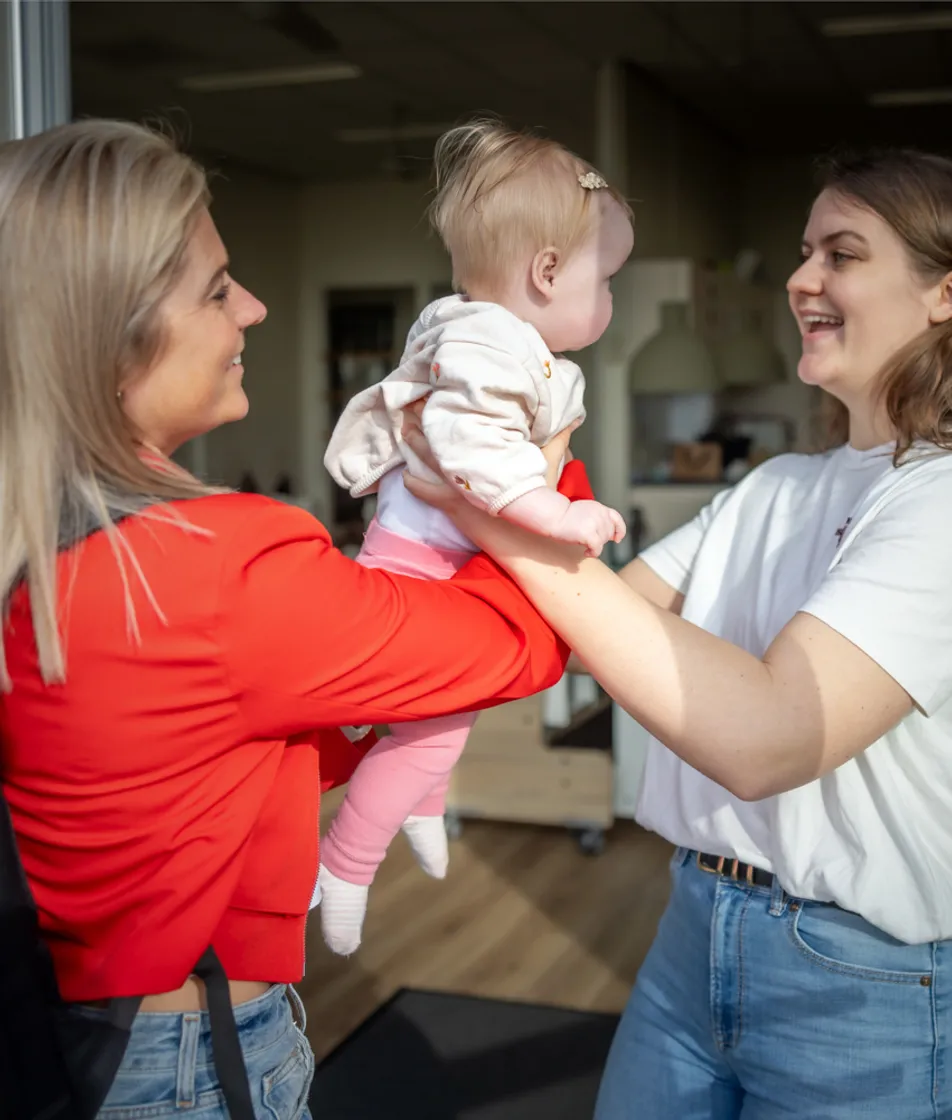 Baby wordt door de moeder aan de pedagogisch medewerker gegeven bij kinderopvang Kind&co ludens