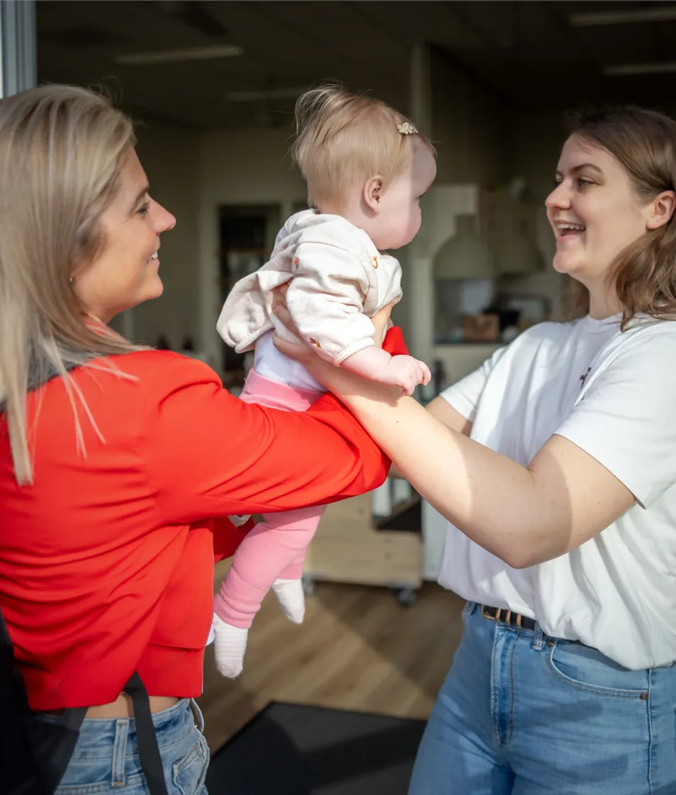 Baby wordt door de moeder aan de pedagogisch medewerker gegeven bij kinderopvang Kind&co ludens