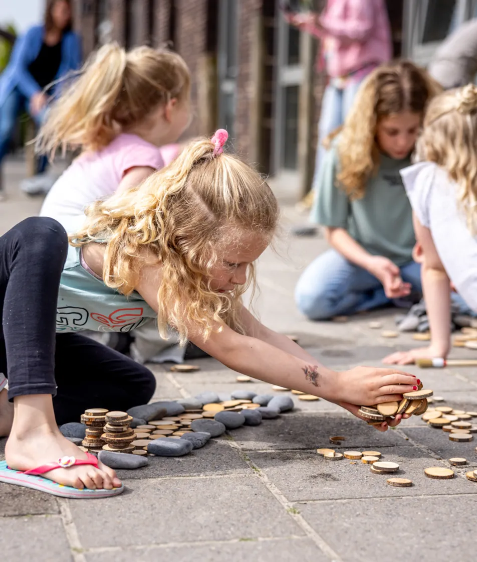 Kinderen spelen buiten op de grond bij kinderopvang Kind&co ludens