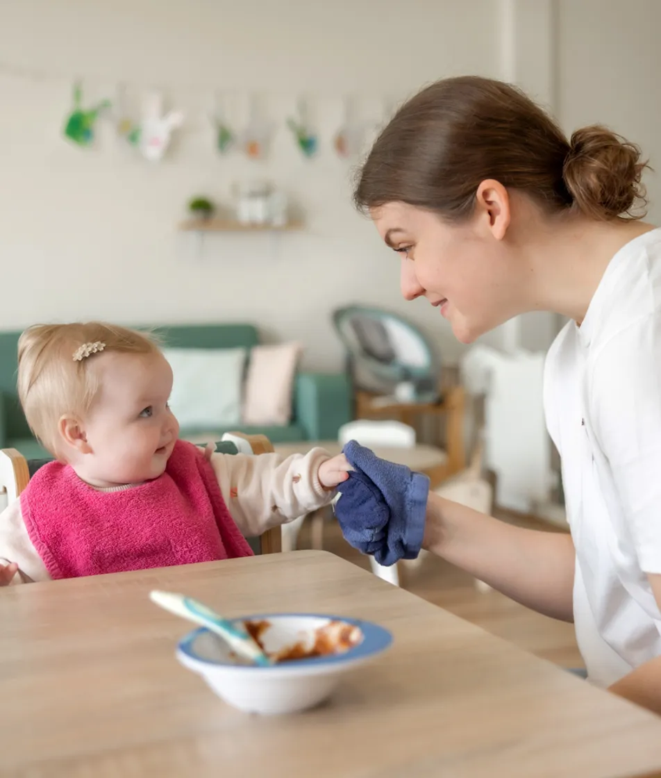 kindje wordt geholpen bij het eten door een pedagogisch medewerker bij kinderopvang Kind&co ludens