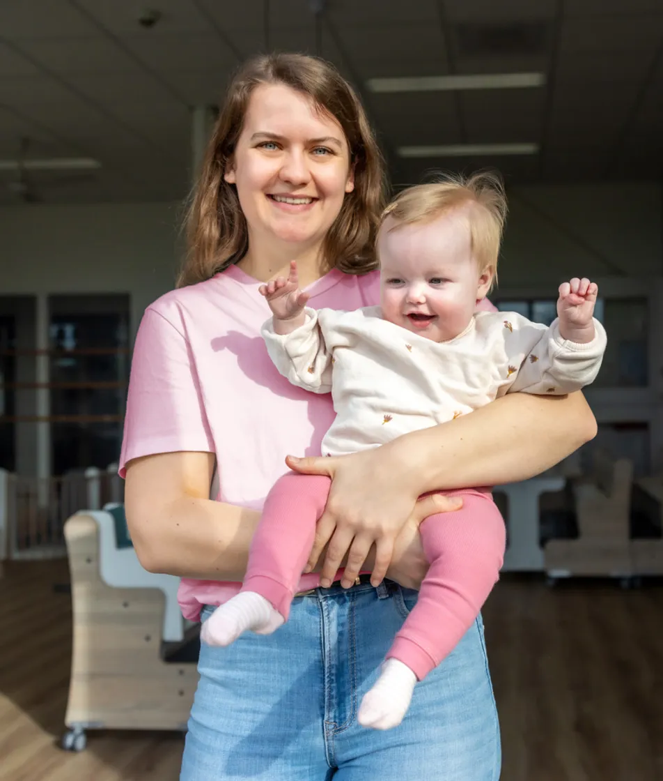 Blij kind op de armen bij een pedagogisch medewerker bij kinderopvang Kind&co ludens