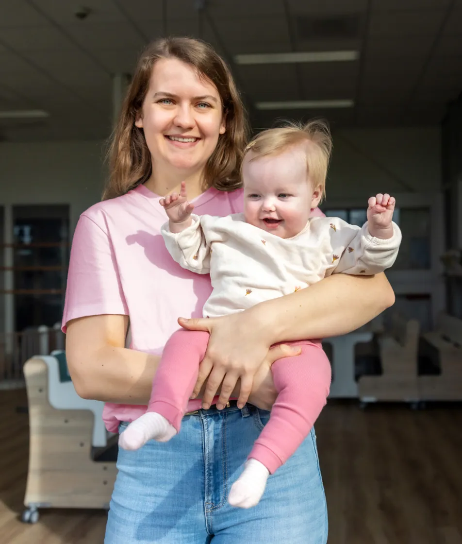Blij kind op de armen bij een pedagogisch medewerker bij kinderopvang Kind&co ludens
