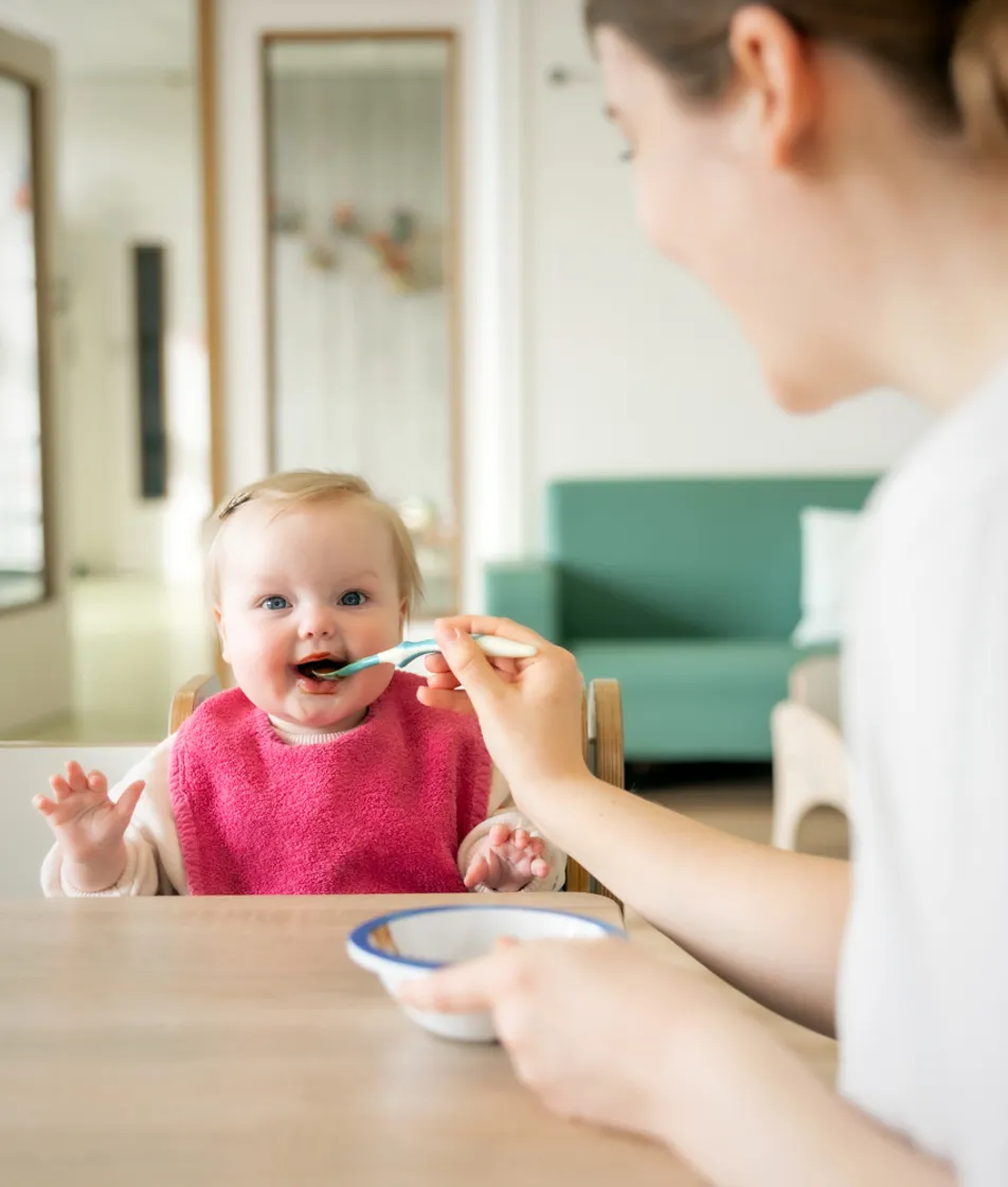 kindje wordt geholpen bij het eten door een pedagogisch medewerker bij kinderopvang Kind&co ludens