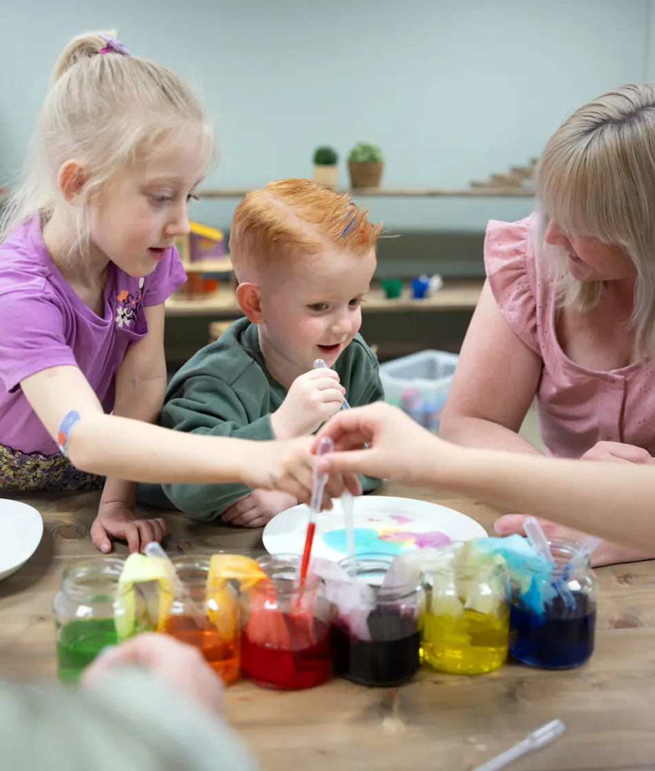 kinderen worden door een pedagogisch medewerker begeleid met het verven bij kinderopvang Kind&co ludens