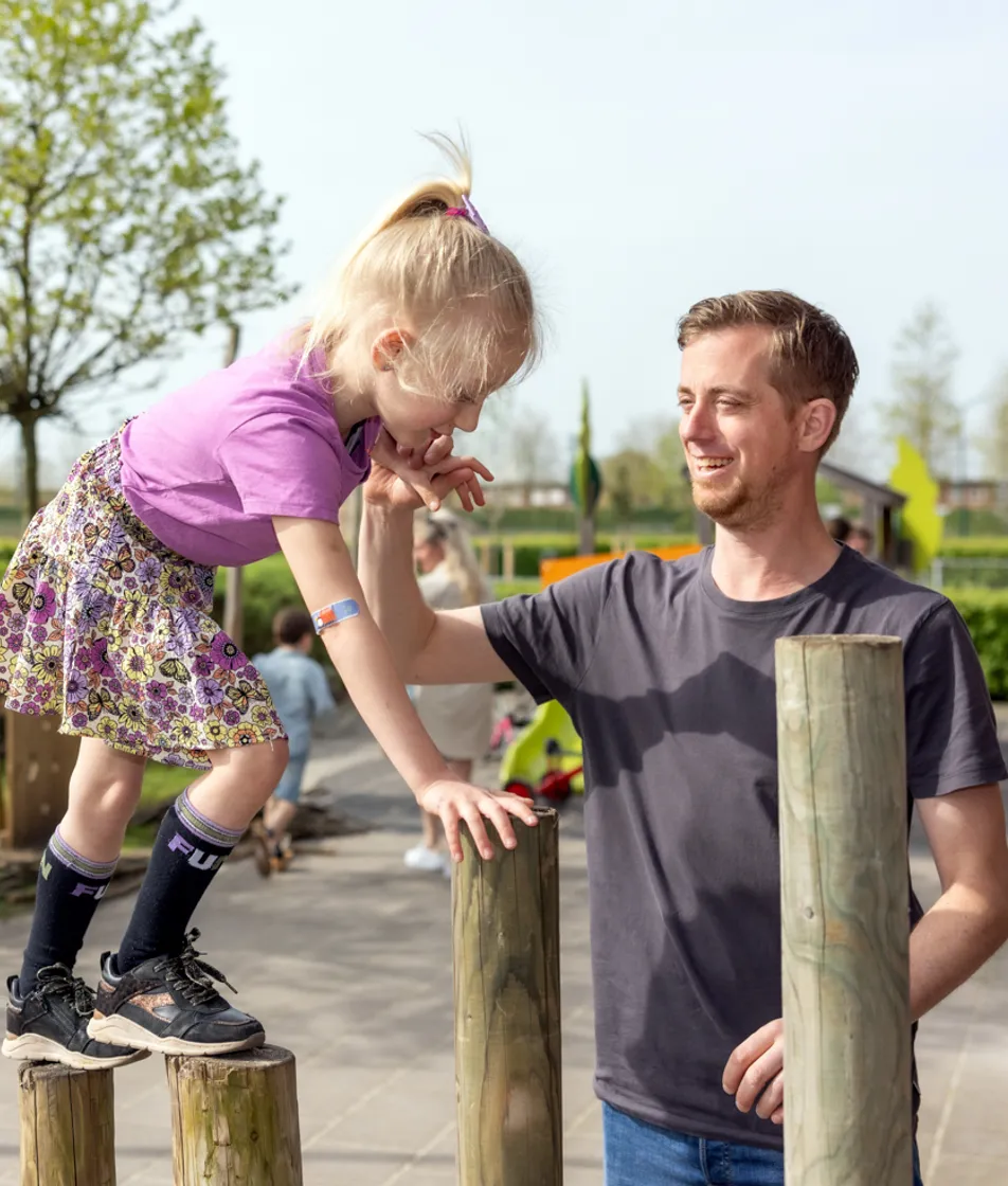 kind wordt begeleid door pedagogisch medewerker bij buitenspelen op palen bij kinderopvang Kind&co ludens