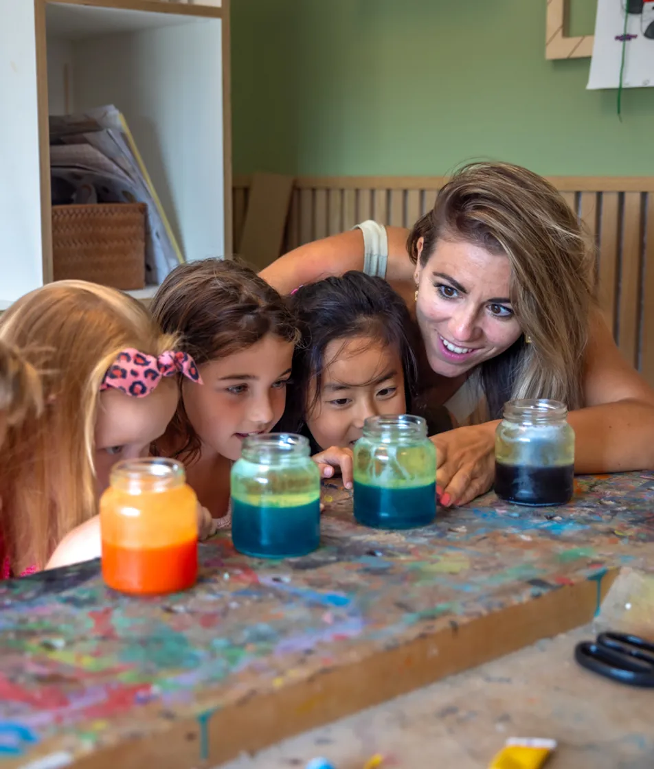 Kinderen kijken met pedagogisch medewerker naar pot met gekleurd water bij kinderopvang Kind&co ludens