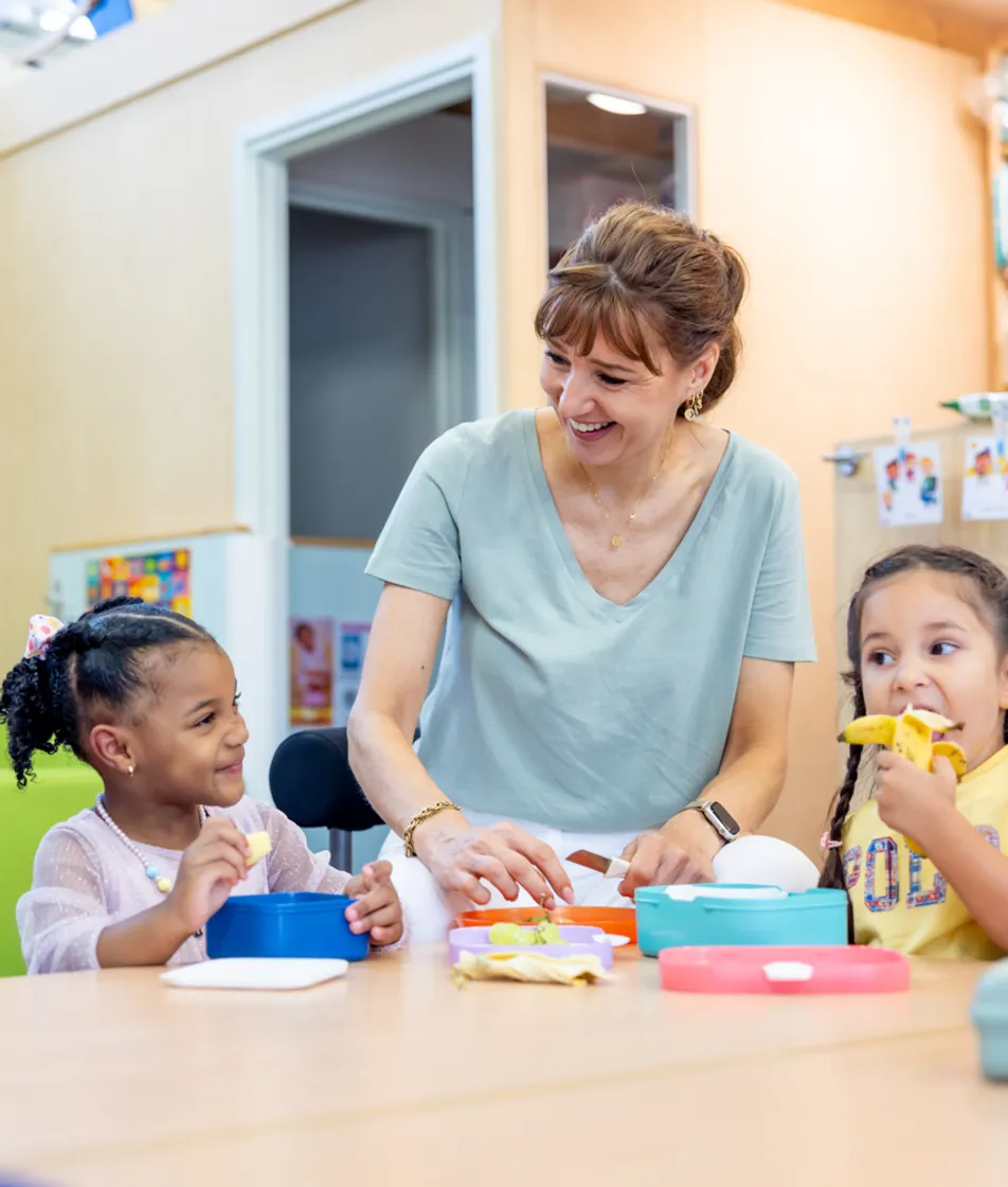 Kinderen eten samen met pedagogisch medewerker aan tafel bij kinderopvang Kind&co ludens