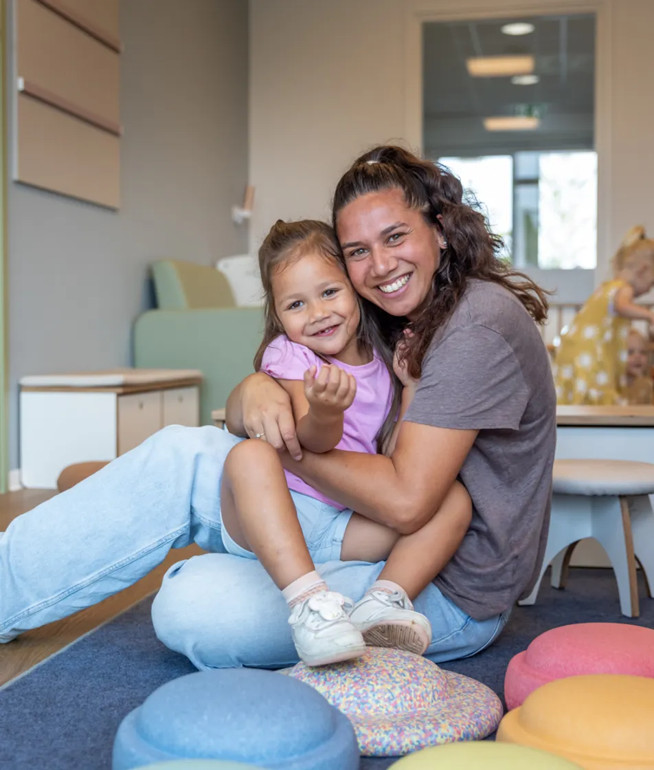 Kind en pedagogisch medewerker knuffelen bij kinderopvang Kind&co ludens