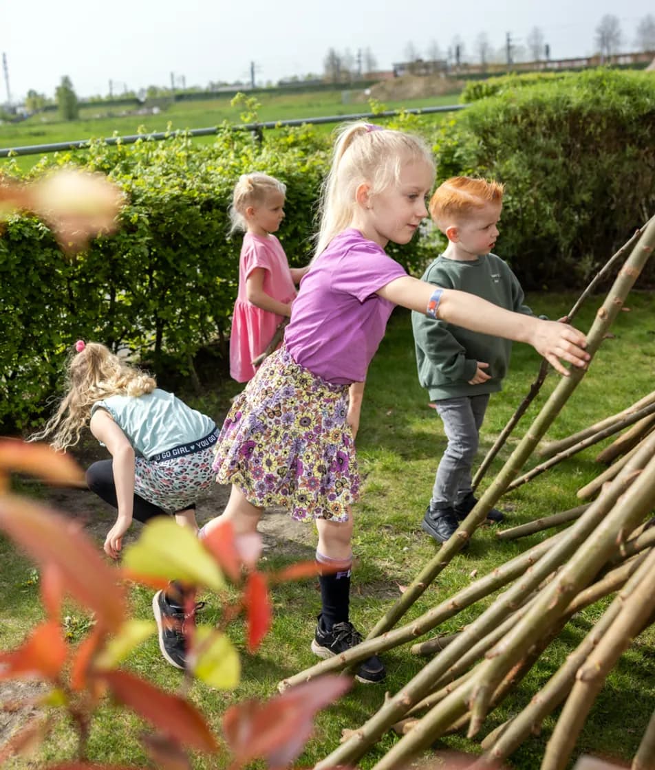 Kinderen bouwen een hut van takken bij kinderopvang Kind&co ludens