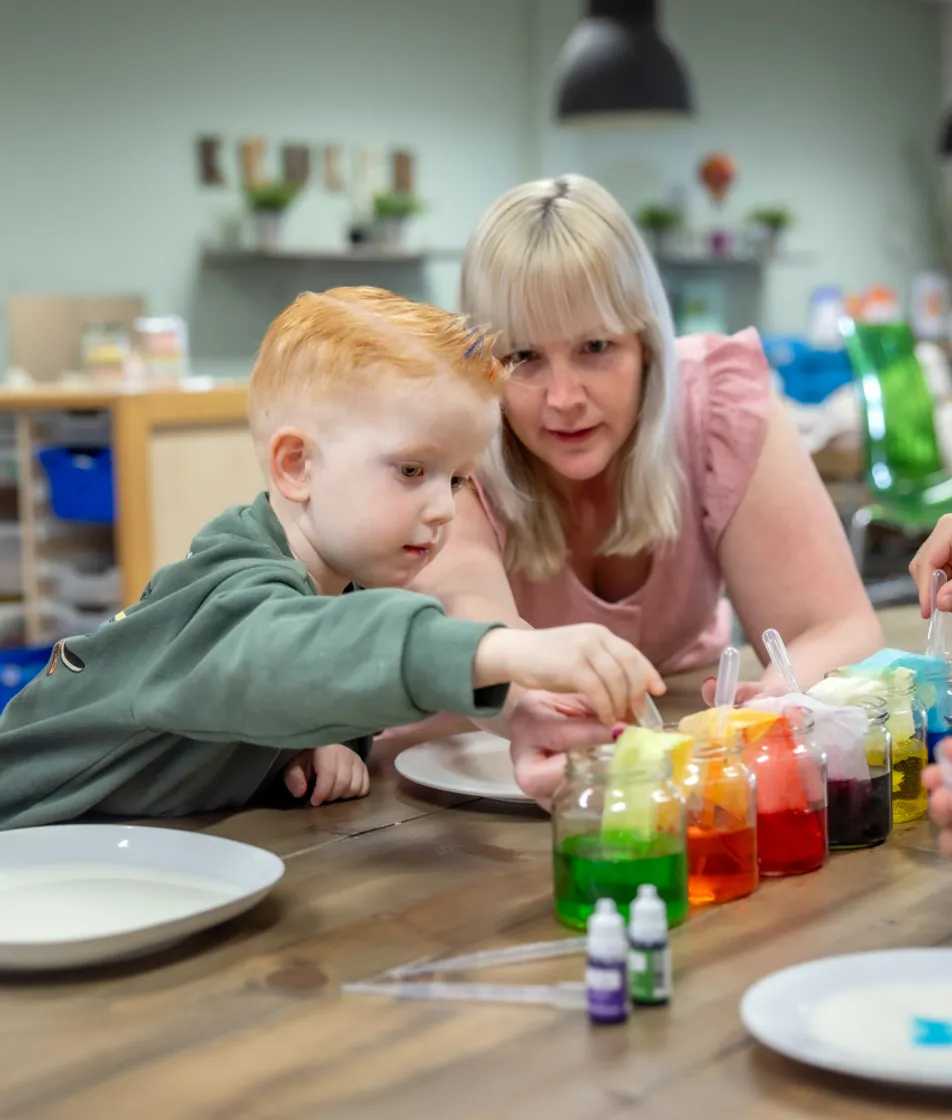 kinderen worden door een pedagogisch medewerker begeleid met het verven bij kinderopvang Kind&co ludens