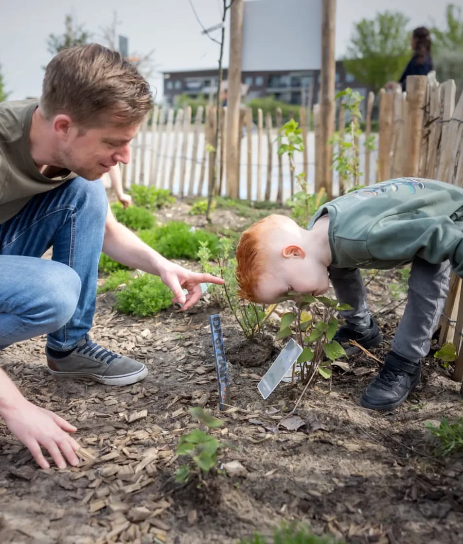Kind ruikt aan bloem in tuin met pedagogisch medewerker bij kinderopvang Kind&co ludens