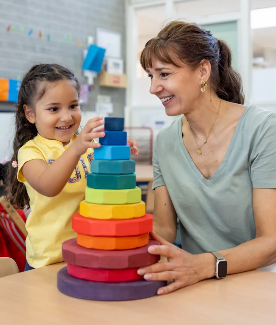 Kind stapelt houten ringen samen met pedagogisch medewerker bij kinderopvang Kind&co ludens