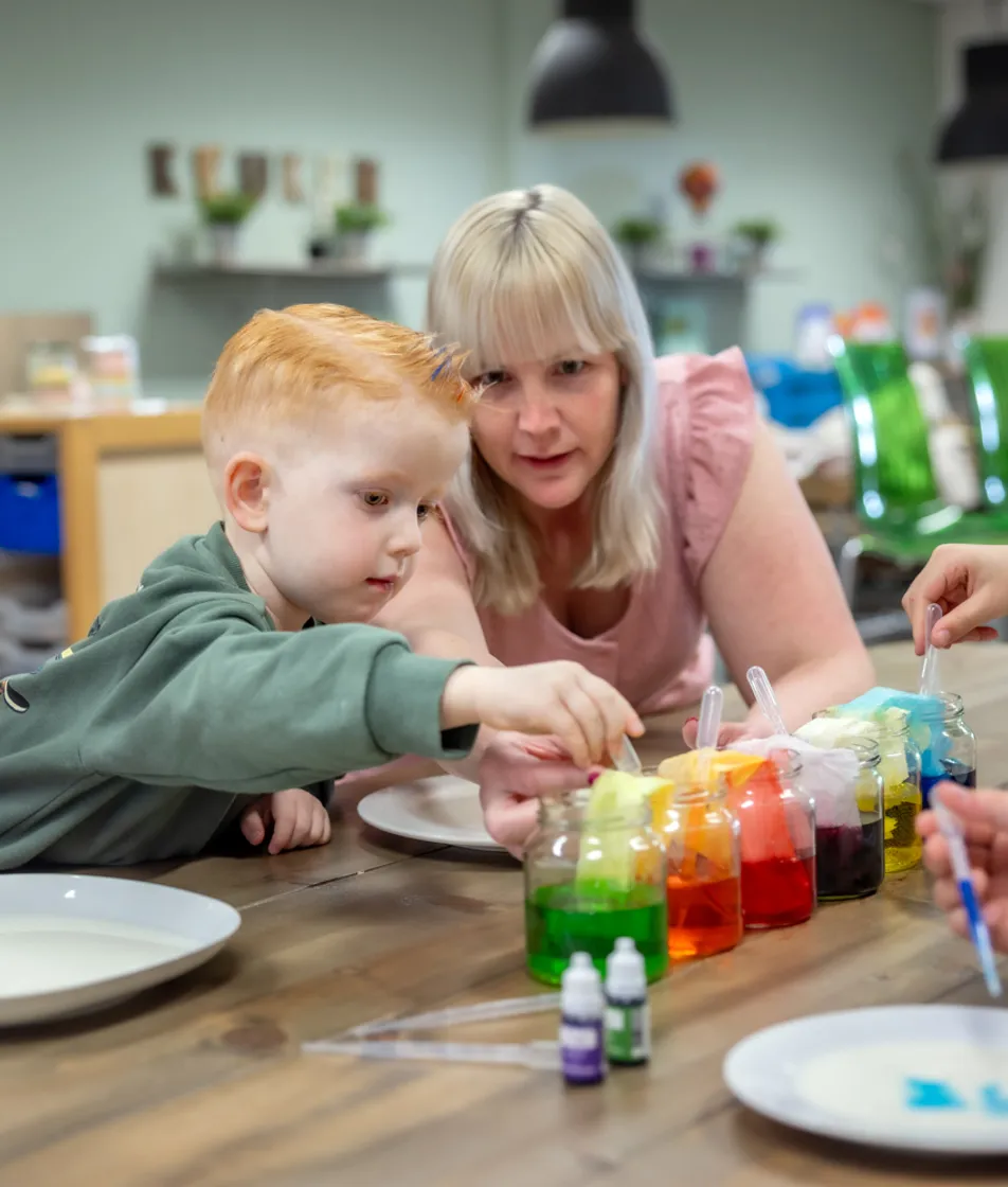 kinderen worden door een pedagogisch medewerker begeleid met het verven bij kinderopvang Kind&co ludens