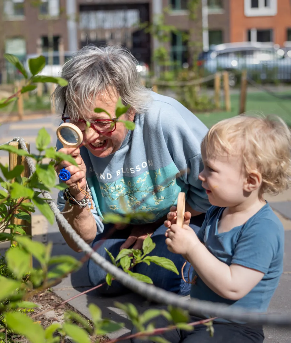 Pedagogisch medewerker en kind kijken samen door een loep naar blaadjes bij kinderopvang Kind&co ludens