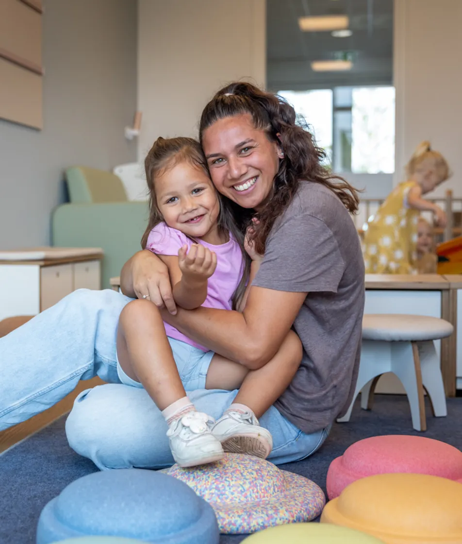 Kind en pedagogisch medewerker knuffelen bij kinderopvang Kind&co ludens