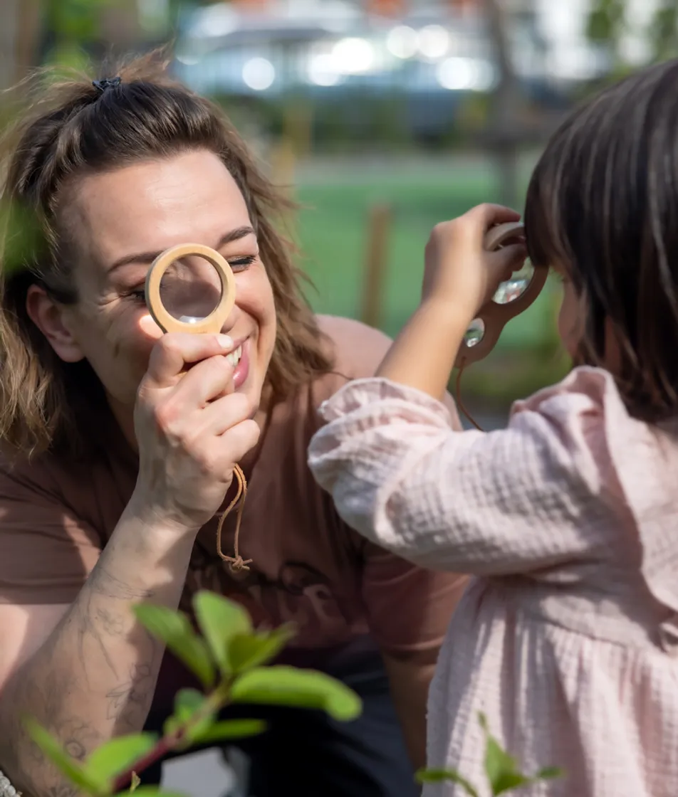 Pedagogisch medewerker en kind kijken samen door een vergrootglas bij kinderopvang Kind&co ludens
