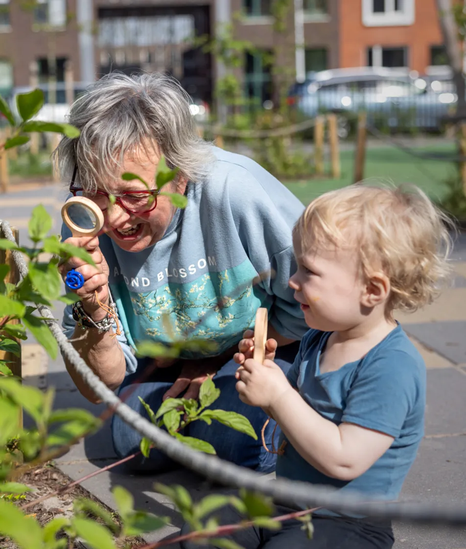 Pedagogisch medewerker en kind kijken samen door een loep naar blaadjes bij kinderopvang Kind&co ludens