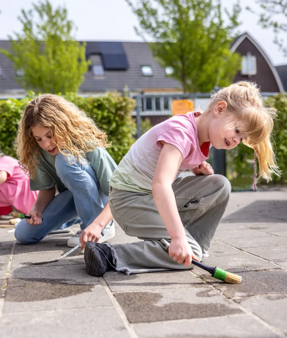 Kinderen spelen buiten op de grond met water bij kinderopvang Kind&co ludens