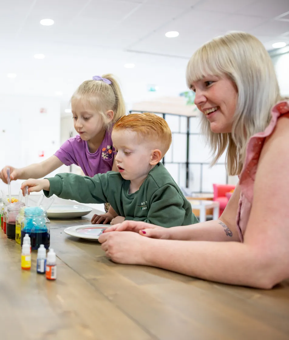 kinderen worden door een pedagogisch medewerker begeleid met het verven bij kinderopvang Kind&co ludens