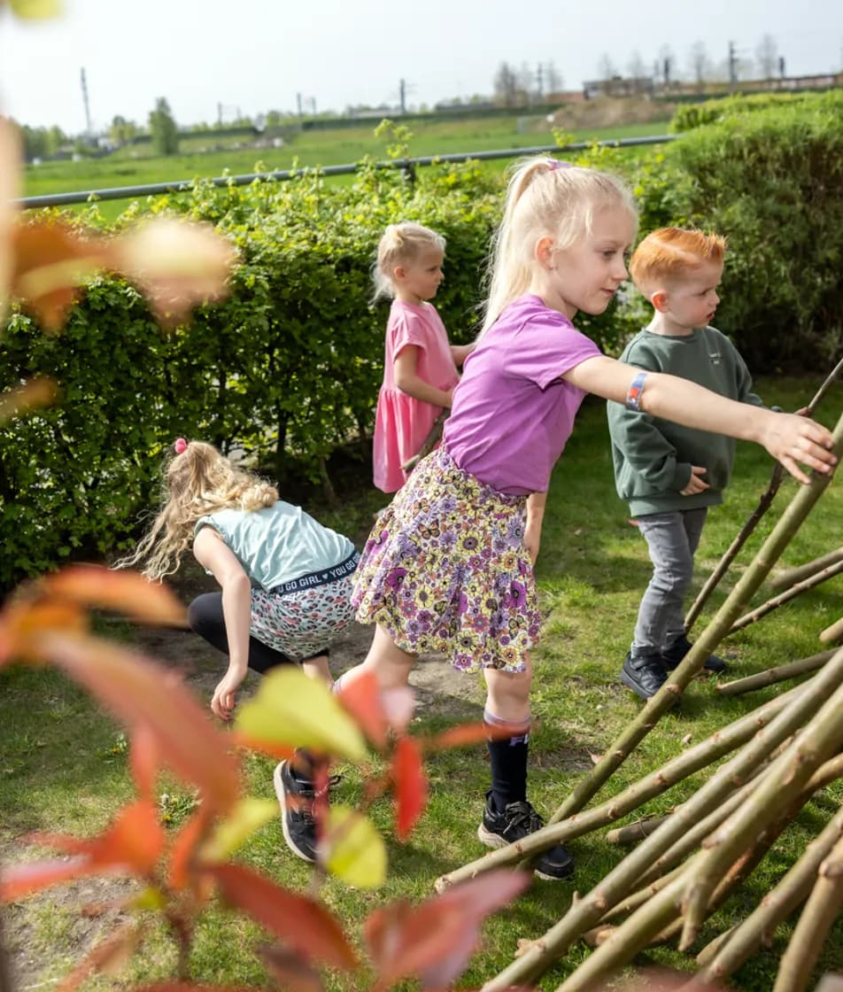 Kinderen bouwen een hut van takken bij kinderopvang Kind&co ludens