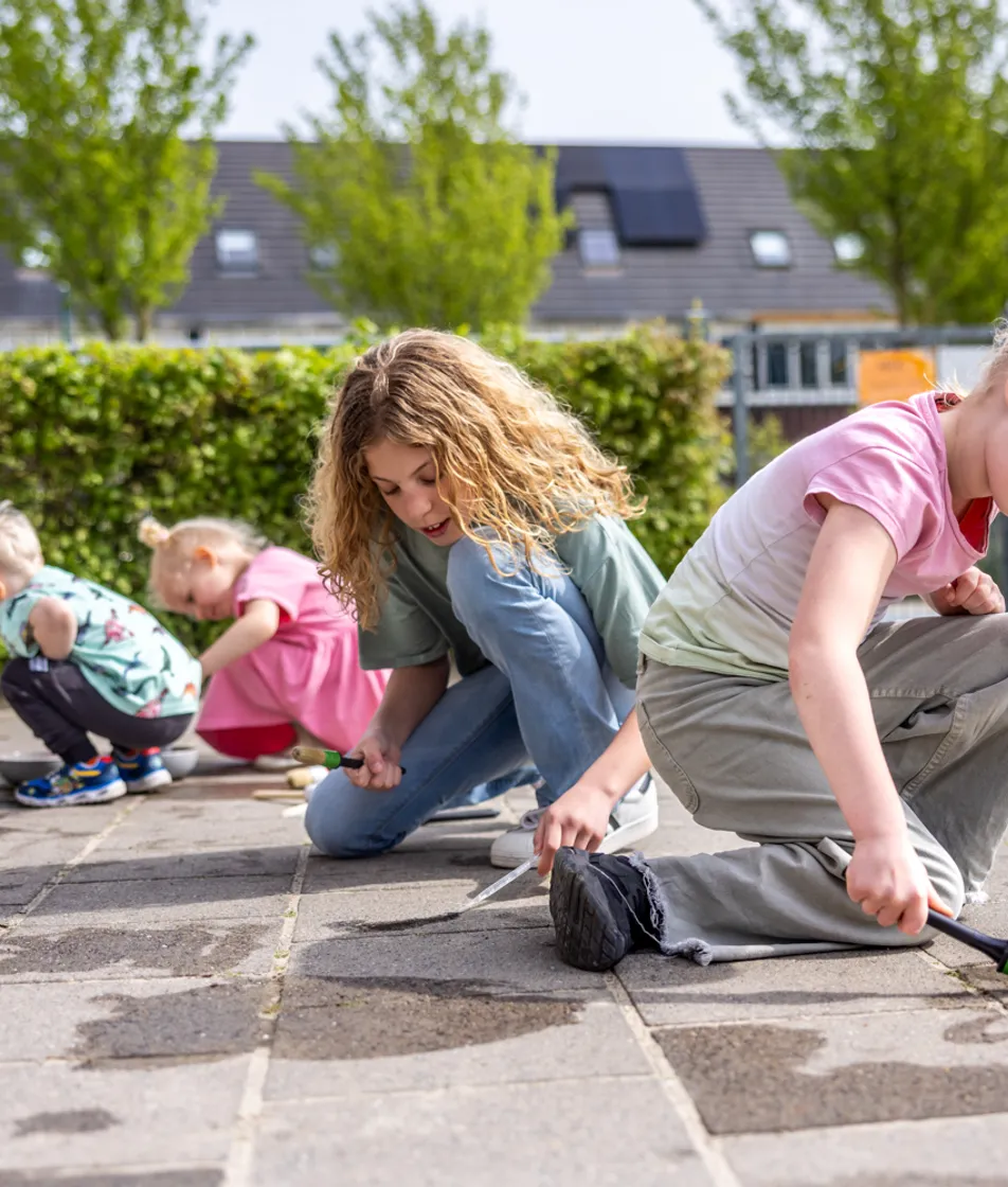 Kinderen spelen buiten op de grond met water bij kinderopvang Kind&co ludens