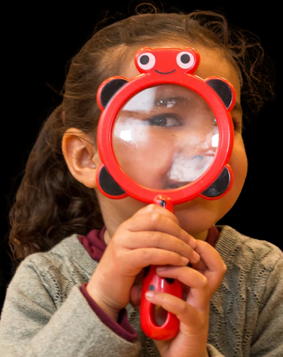 Kind kijkt door vergrootglas bij kinderopvang Kind&co ludens