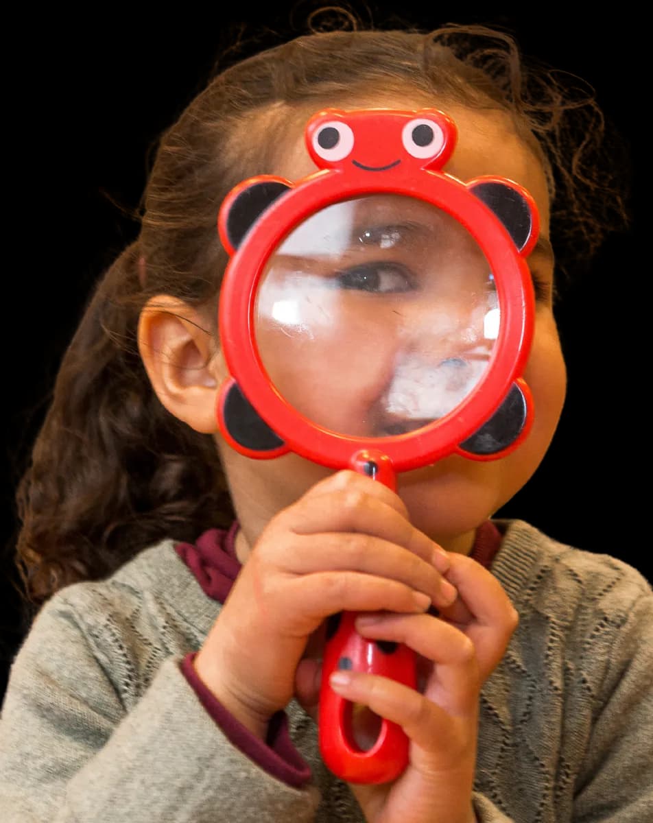 Kind kijkt door vergrootglas bij kinderopvang Kind&co ludens
