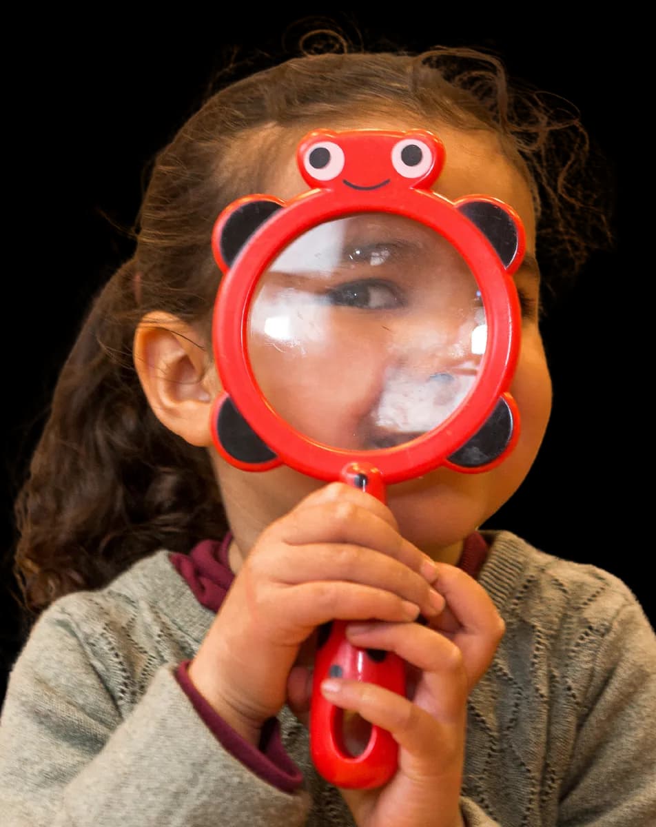 Kind kijkt door vergrootglas bij kinderopvang Kind&co ludens