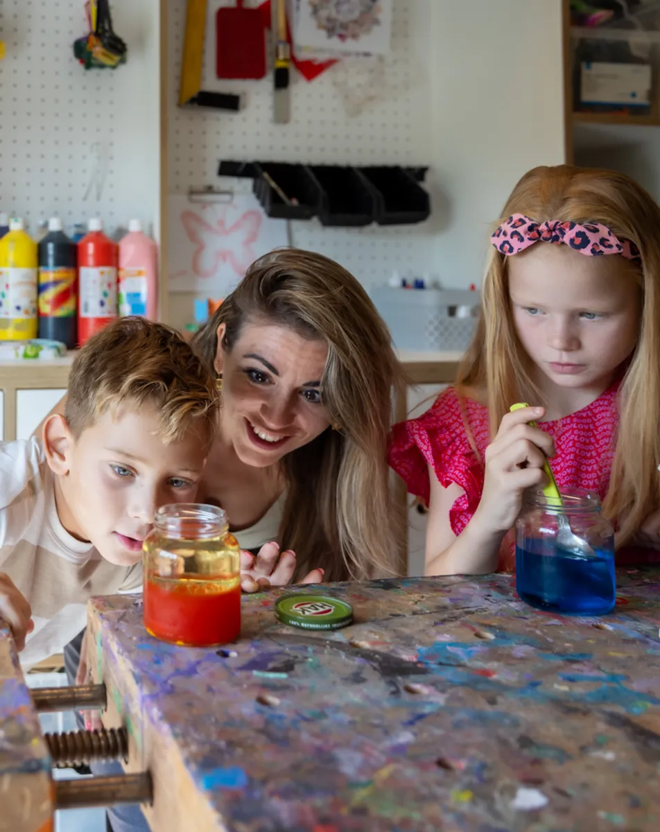 Kinderen kijken met pedagogisch medewerker naar pot met gekleurd water bij kinderopvang Kind&co ludens